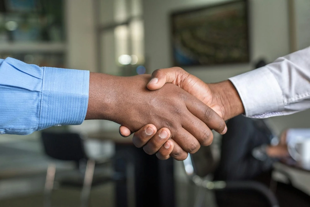 Two Black people shaking hands (only arms are visible)