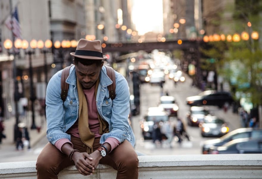 A black man looks down while sitting on an overpass