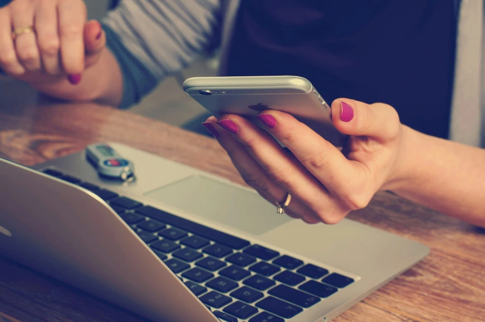 Detail of a person looking at their phone over their laptop